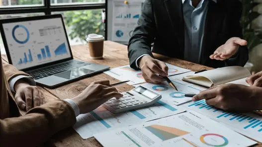 Bilanzkreismanagement von erneuerbaren Energien Drei Personen sitzen an einem Tisch, auf dem Blätter mit verschiedenen Statistiken liegen ebenso wie ein Laptop.