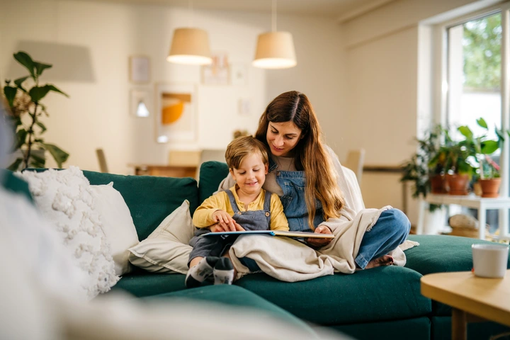 Gemütliche Lesestunde zu Hause Mutter und Sohn sitzen gemütlich auf dem Sofa und schauen sich ein Bilderbuch an. Das Wohnzimmer ist mit Pflanzen dekorativ geschmückt