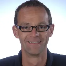 Portraitfoto einer männliche Person mit Brille und dunkelblauen Oberteil auf weißem Hintergrund 