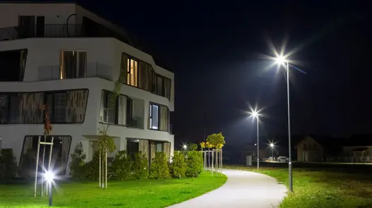 Effiziente Straßen- und Wegebeleuchtung Ein modernes Wohngebäude bei Nacht mit beleuchtetem Weg und Straßenlaternen.