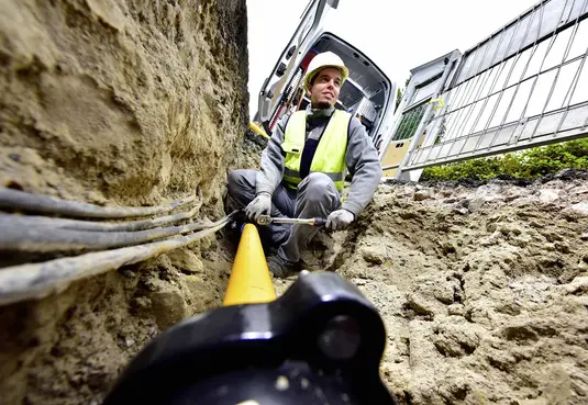 Monteur in einem Kabelgraben mit Warnweste und Helm