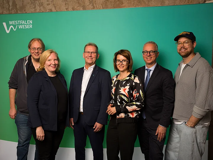 Die Jurymitglieder Sechs Mitglieder der Jury vom WWKulturSTARTER26 stehen vor einer grünen Westfalen-Weser-Fotowand.