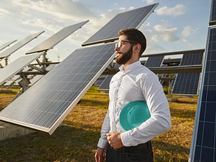 Photovoltaikanlagen für Unternehmen Ein lächelnder Mann mit Hemd hat seine Brille in der Hand und steht vor Photovoltaikanlagen auf einem Feld.