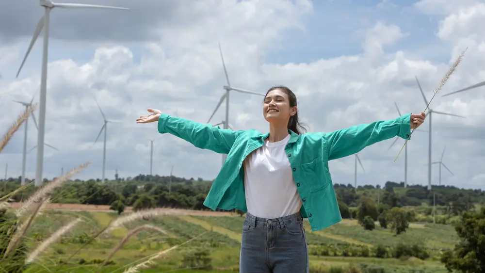 Junge Frau genießt die Sonne und im Hintergrund sind Windräder.