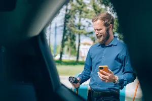 Flexible Vermarktung der Ladeinfrastruktur Eine Person steht im Freien und hält ein Ladekabel sowie ein Smartphone neben einer Ladesäule.