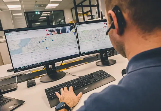 Person sitz arbeitend an einem Schreibtisch vor zwei PC-Bildschirmen an der Tastatur