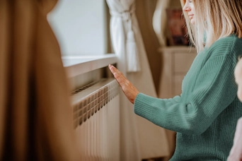 Frau an der Heizung Eine Frau wärmt sich die Hand an der Heizung in einem gemütlichen Wohnzimmer