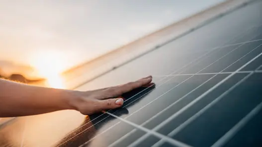 Virtuelle Verrechnungsbilanzkreise bei erneuerbaren Energien Eine Hand liegt auf einem PV-Modul und im Hintergrund geht die Sonne langsam unter.