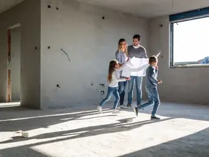 Familie im Neubau Eine Familie steht im Rohbau. Die Kinder spielen und die Eltern halten einen Plan in den Händen