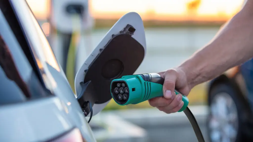 Eine Hand hält einen grünen Ladestecker und verbindet ihn mit einem Elektrofahrzeug.