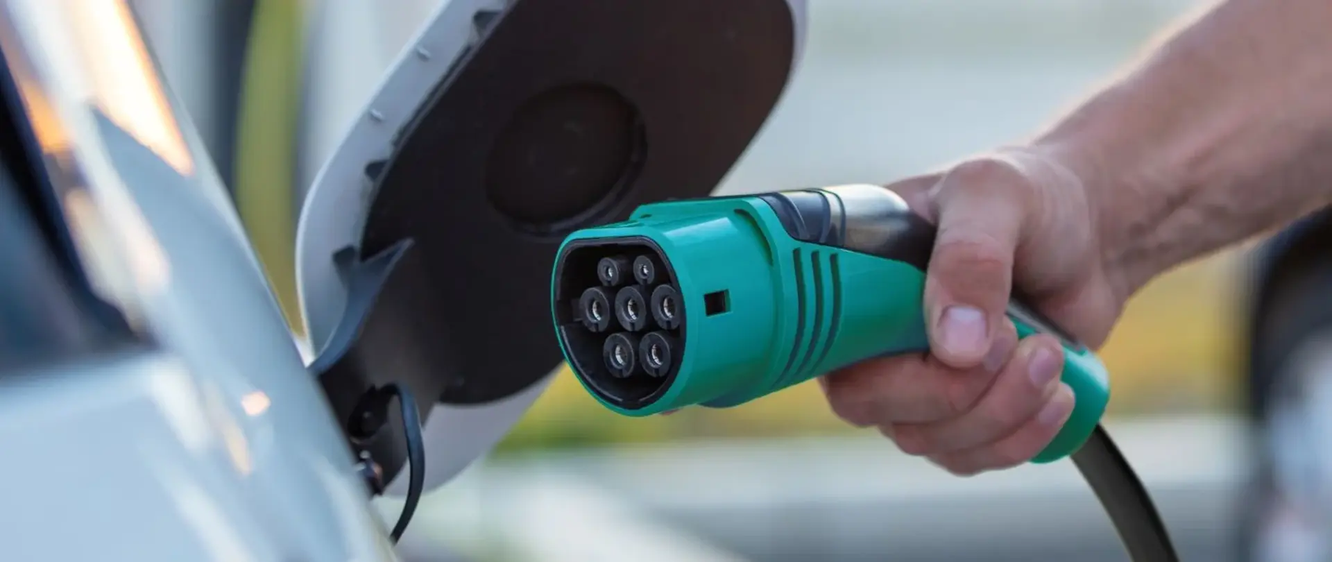 Eine Hand hält einen grünen Ladestecker und verbindet ihn mit einem Elektrofahrzeug.
