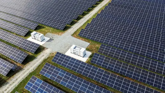 Solarpark mit netzdienlichen Batteriespeichern Eine große Solaranlage mit Batteriespeichern und Schotterweg verläuft durch grüne Flächen mit Solarpaneelen.