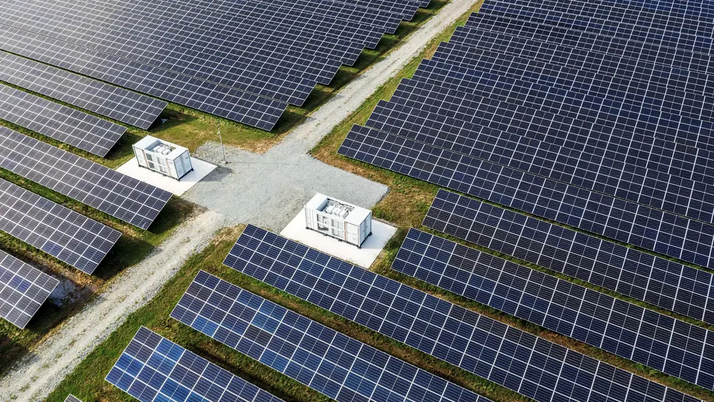 Eine große Solaranlage mit Batteriespeichern und Schotterweg verläuft durch grüne Flächen mit Solarpaneelen.