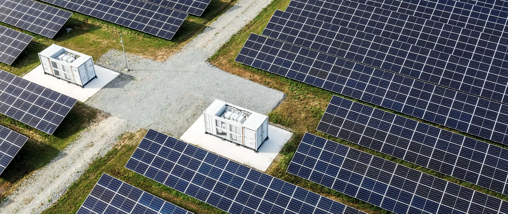 Eine große Solaranlage mit Batteriespeichern und Schotterweg verläuft durch grüne Flächen mit Solarpaneelen.