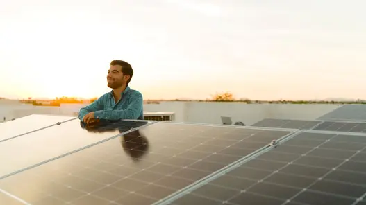 Direktvermarktung von erneuerbaren Energien Ein Mann steht hinter einer großen PV-Anlage auf einer Wiese und schaut bei einem Sonnenuntergang in die Ferne.