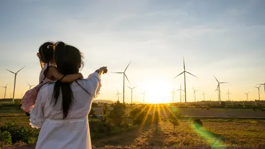 Redispatch 2.0 bei Windpark Eine Mutter hat ihre Tochter auf dem Arm und zeigt auf einen Windpark im Hintergrund beim Sonnenuntergang.
