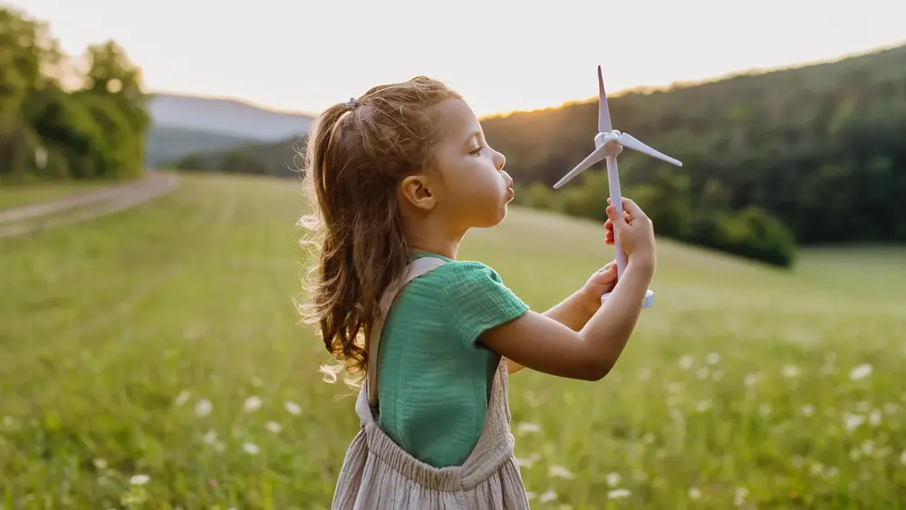 Kleines Mädchen auf der Wiese hält ein Windradmodell in den Händen.