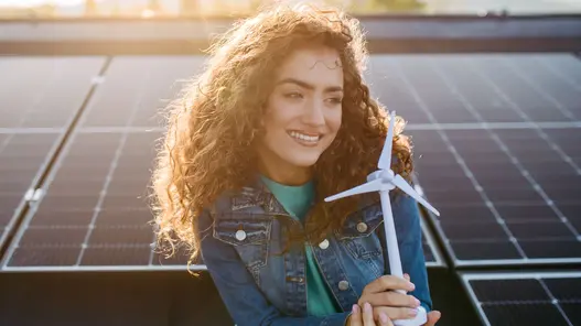 Energievermarktung von erneuerbaren Energien Eine Person hält ein Windturbinenmodell vor Solarpaneelen und symbolisiert nachhaltige Energieerzeugung.