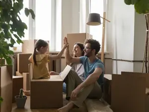 Familie im Umzug Eine dreiköpfige Familie sitzt im Wohnzimmer ihrer neuen Wohnung umringt von Kartons. Der Vater und das Kind klatschen ein