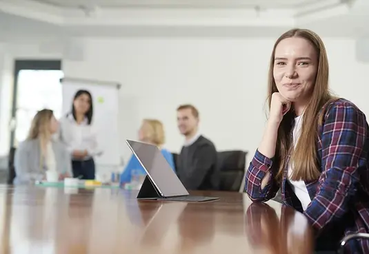 Bild mit einer weiblichen Person sitzend im Vordergrund im Hintergrund weitere Personen in Business Kleidung