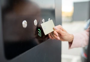 Kontaktloses Bezahlen für Ladeinfrastruktur Eine Person hält eine Karte vor ein kontaktloses Zahlungsterminal mit grünem Signal-Icon.